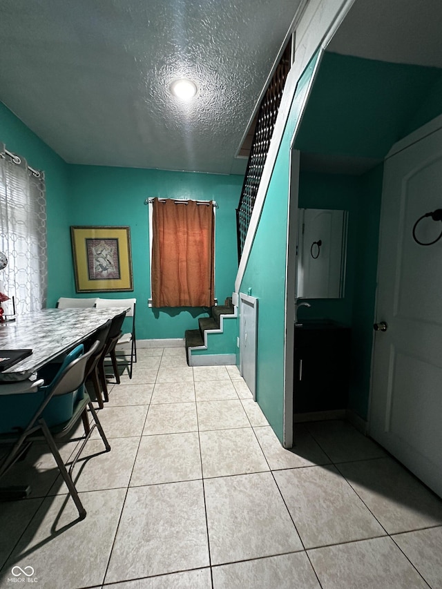 interior space featuring light tile patterned floors, a textured ceiling, and baseboards