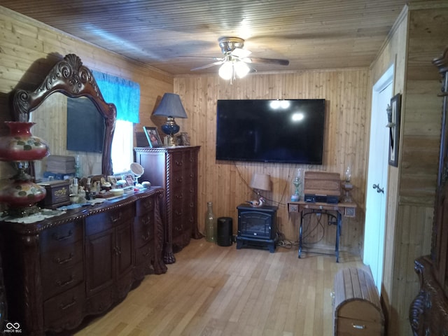 interior space with wooden ceiling, wooden walls, wood finished floors, a ceiling fan, and a wood stove