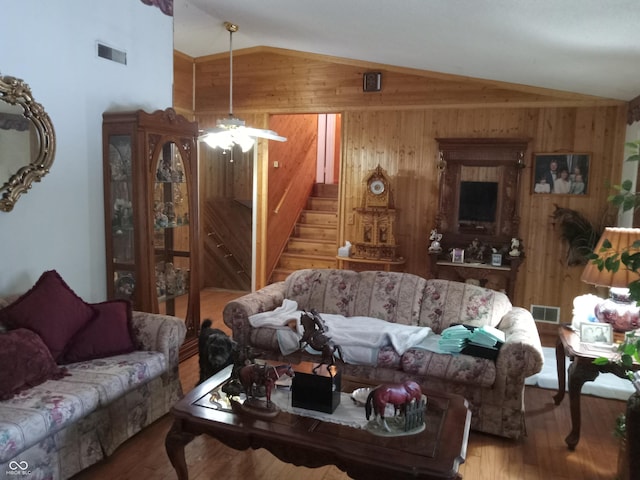 living area with visible vents, vaulted ceiling, wood walls, and wood finished floors