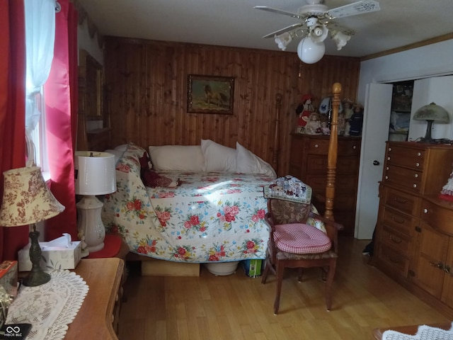 bedroom with ceiling fan, light wood finished floors, and wooden walls