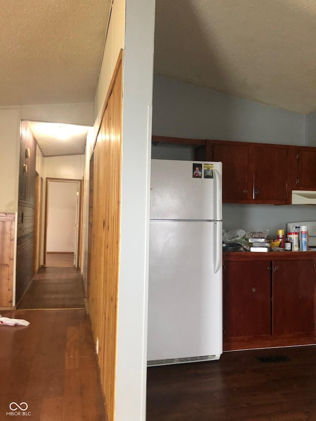 kitchen featuring vaulted ceiling, dark wood-style flooring, freestanding refrigerator, and range hood