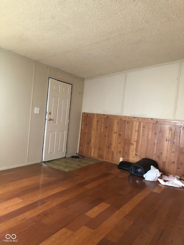 spare room featuring a wainscoted wall, wooden walls, a textured ceiling, and wood finished floors