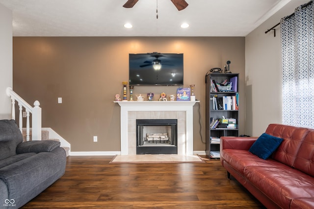 living room with baseboards, dark wood finished floors, a tile fireplace, ceiling fan, and stairway