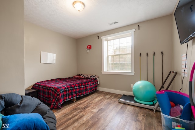 bedroom featuring baseboards, a textured ceiling, visible vents, and wood finished floors