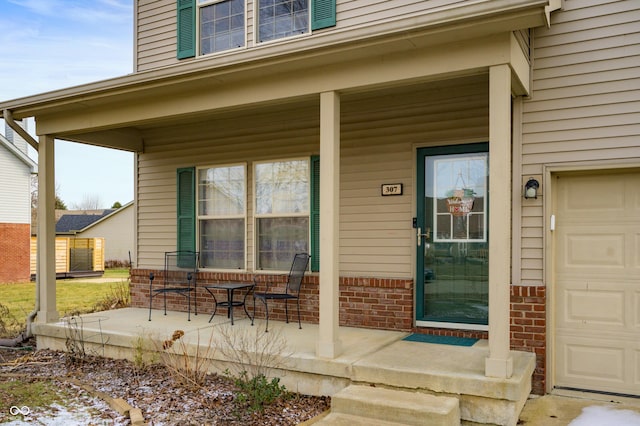 doorway to property with a garage, covered porch, and brick siding