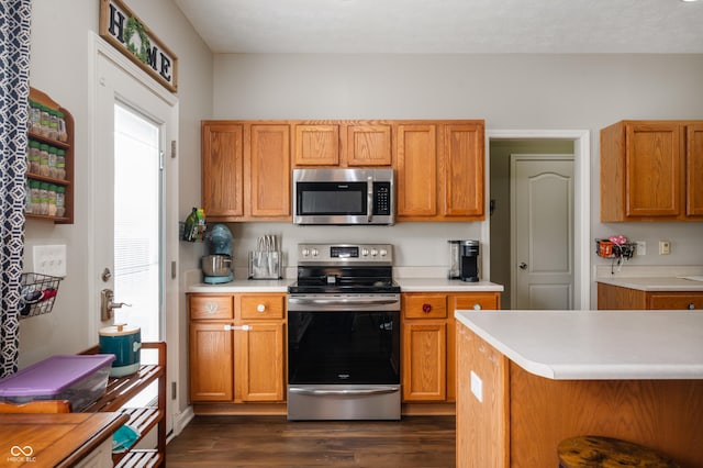 kitchen featuring light countertops, appliances with stainless steel finishes, dark wood-style flooring, and brown cabinetry