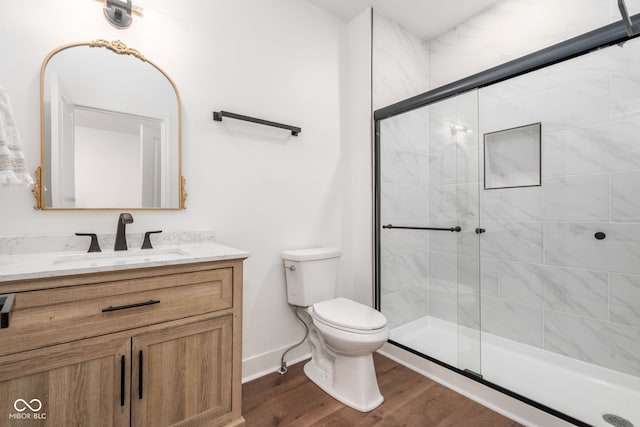 bathroom with toilet, wood finished floors, vanity, baseboards, and a shower stall