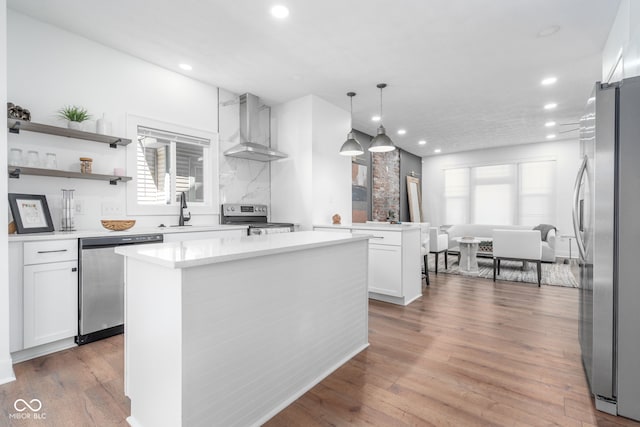 kitchen featuring a wealth of natural light, wall chimney range hood, a sink, and appliances with stainless steel finishes