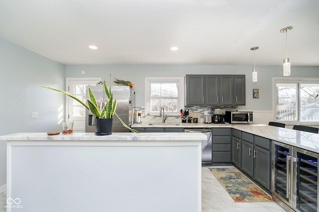 kitchen featuring pendant lighting, gray cabinets, appliances with stainless steel finishes, a sink, and a peninsula