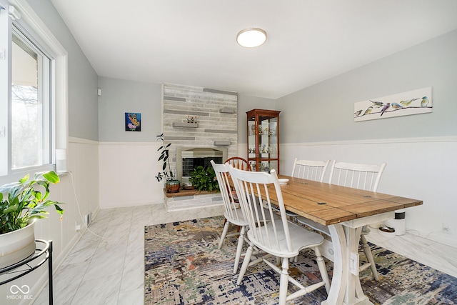 dining room with a large fireplace, wainscoting, and marble finish floor