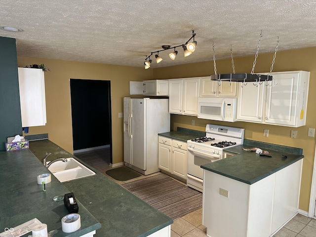 kitchen with a peninsula, white appliances, a sink, white cabinets, and dark countertops