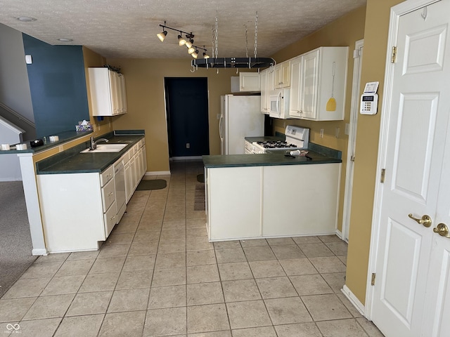 kitchen with white appliances, dark countertops, a peninsula, white cabinetry, and a sink