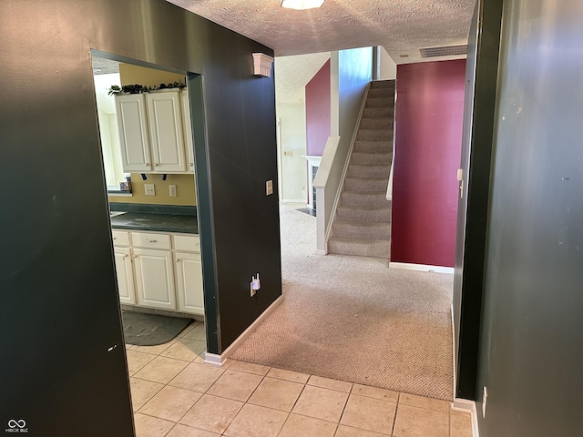 corridor with a textured ceiling, light tile patterned flooring, light carpet, visible vents, and stairs