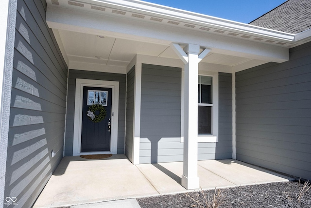 entrance to property with covered porch and a shingled roof