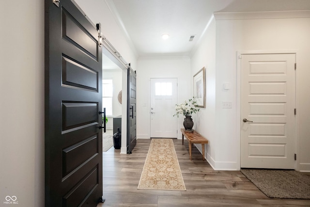 entryway featuring a barn door, baseboards, crown molding, and wood finished floors