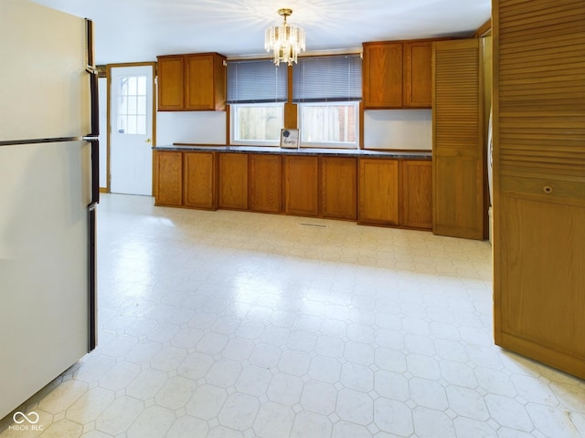 kitchen with brown cabinetry, freestanding refrigerator, decorative light fixtures, and light floors