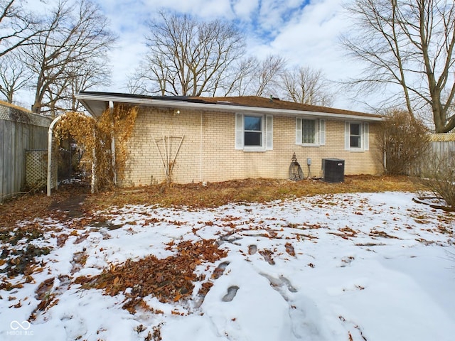 snow covered property with brick siding, cooling unit, and fence