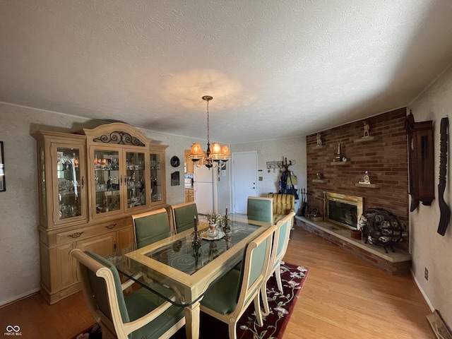 dining room with a brick fireplace, a textured ceiling, a chandelier, and light wood-style floors