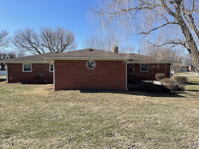 view of side of home featuring brick siding, a lawn, and a chimney