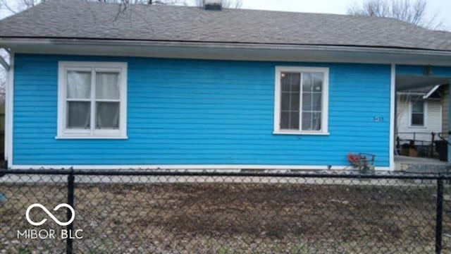 view of side of property with roof with shingles and fence