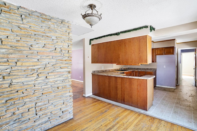 kitchen with baseboards, light wood-style flooring, a peninsula, a textured ceiling, and a sink