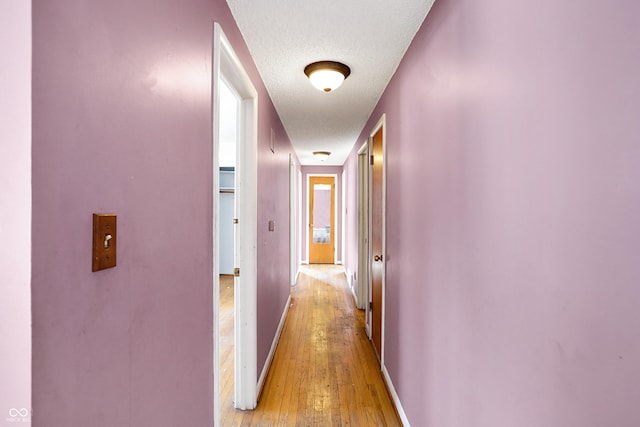 hallway featuring light wood-type flooring, a textured ceiling, and baseboards