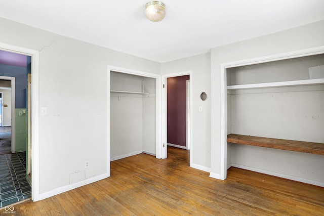 unfurnished bedroom with wood finished floors, two closets, and baseboards