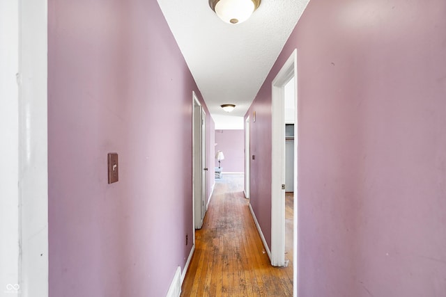 hallway featuring a textured ceiling, baseboards, and wood finished floors