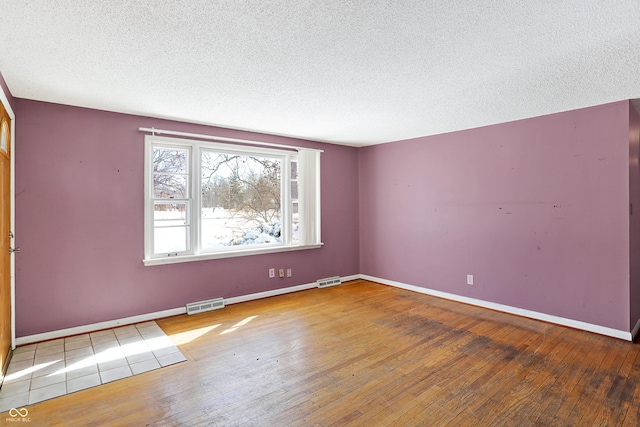 spare room with visible vents, a textured ceiling, baseboards, and wood finished floors