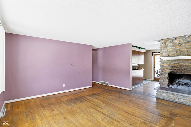 unfurnished living room with a stone fireplace, wood finished floors, visible vents, and baseboards