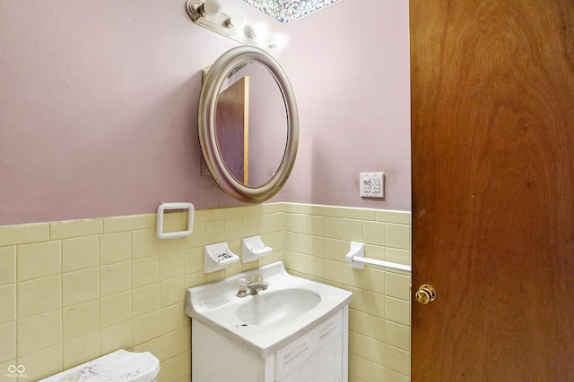 bathroom featuring toilet, vanity, tile walls, and wainscoting