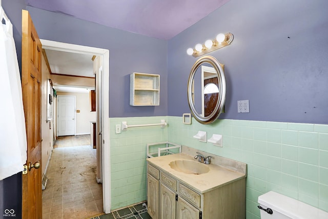 bathroom featuring toilet, a wainscoted wall, tile walls, and vanity