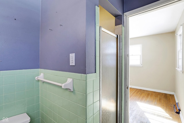 bathroom with tile walls, toilet, wainscoting, a shower stall, and wood finished floors