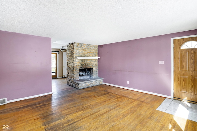 unfurnished living room featuring visible vents, a stone fireplace, a textured ceiling, wood finished floors, and baseboards