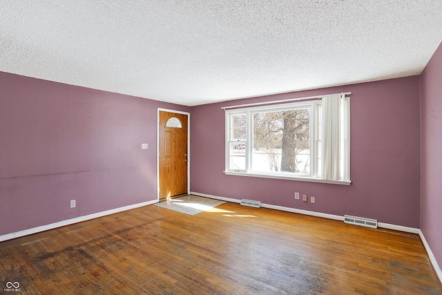 spare room with visible vents, a textured ceiling, baseboards, and wood finished floors