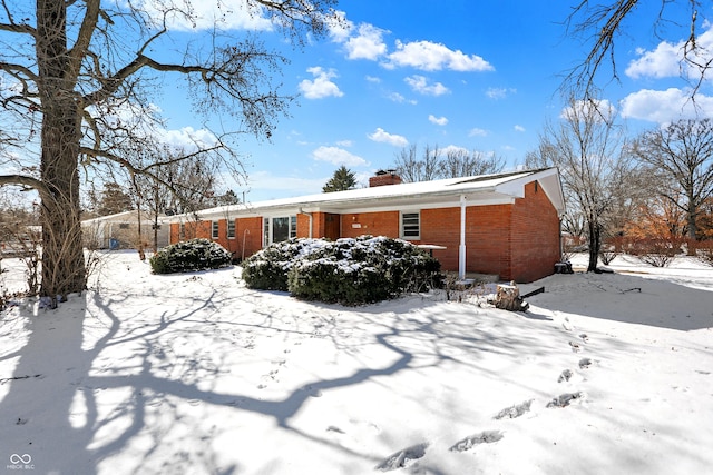 snow covered house with brick siding and a chimney