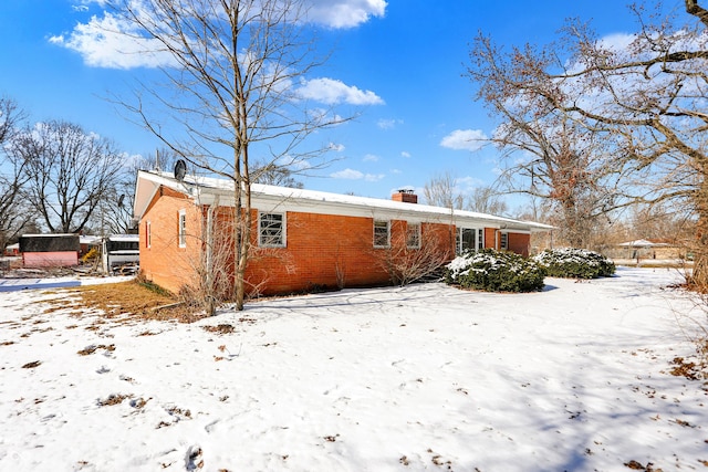 snow covered house with brick siding and a chimney