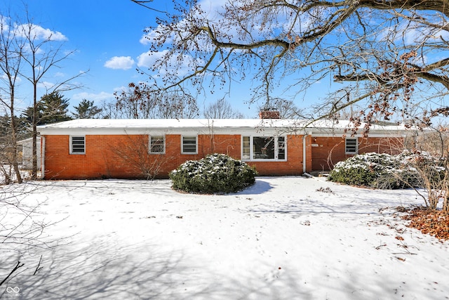 snow covered property featuring a chimney and brick siding