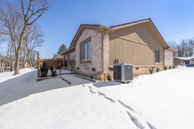 view of snowy exterior featuring brick siding and cooling unit