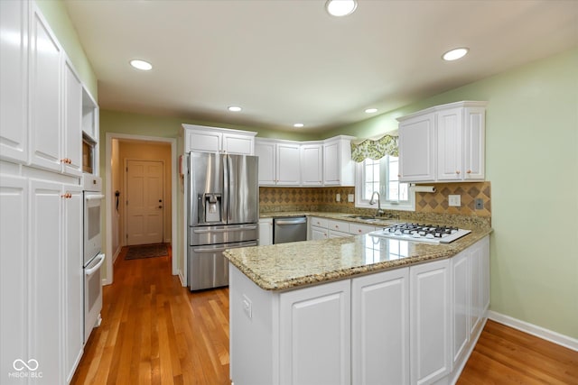 kitchen featuring a peninsula, white appliances, white cabinets, and a sink