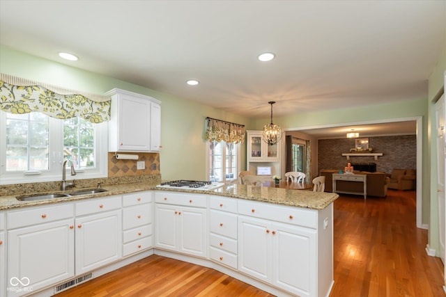 kitchen featuring visible vents, light wood-style flooring, white gas cooktop, a sink, and a peninsula