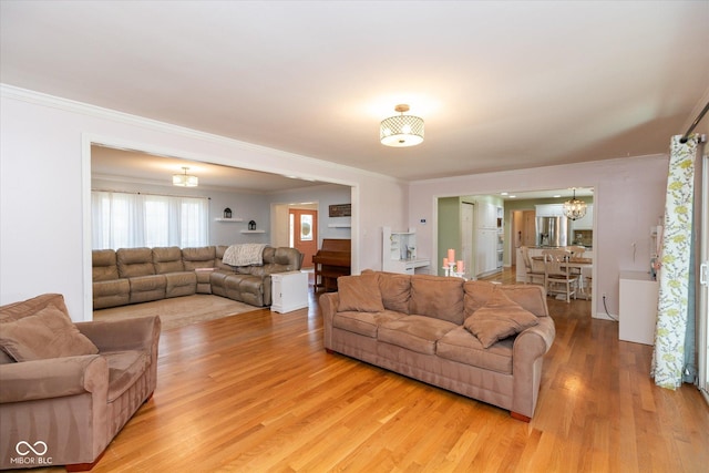 living room with light wood-style floors, crown molding, and an inviting chandelier