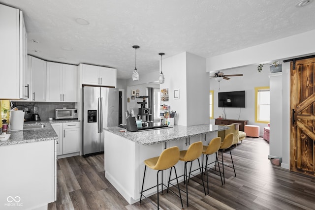 kitchen with dark wood-type flooring, tasteful backsplash, stainless steel fridge with ice dispenser, and a barn door