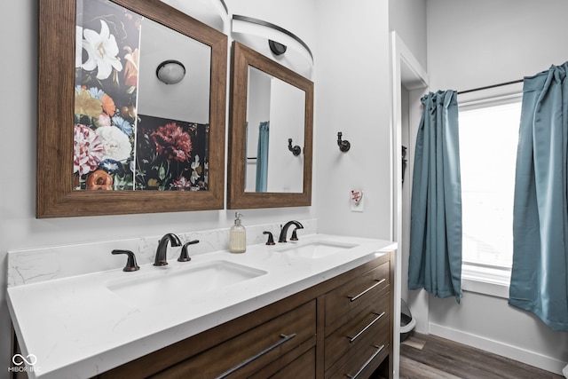 full bath featuring wood finished floors, a sink, baseboards, and double vanity