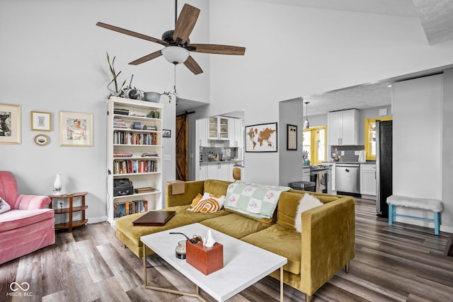 living area with a towering ceiling, a barn door, a ceiling fan, wood finished floors, and baseboards