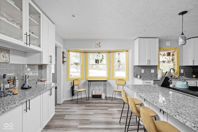 kitchen featuring a breakfast bar, glass insert cabinets, white cabinetry, and light wood-style floors