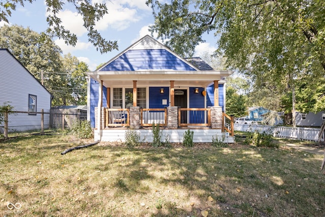 view of front of home with stone siding, a porch, a front yard, and fence