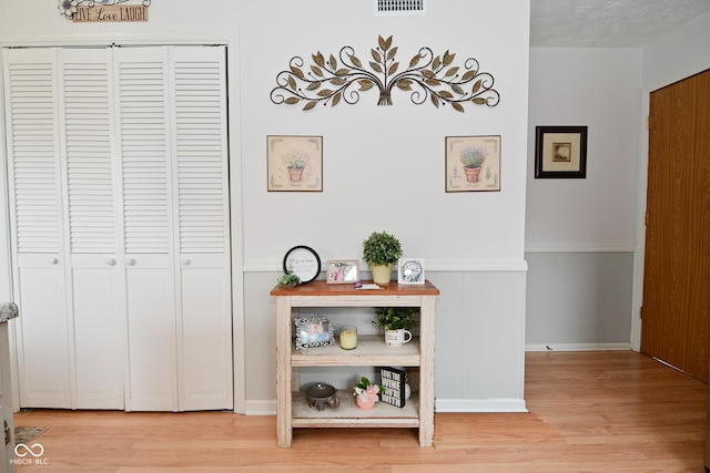 corridor featuring light wood finished floors, baseboards, visible vents, and a textured ceiling