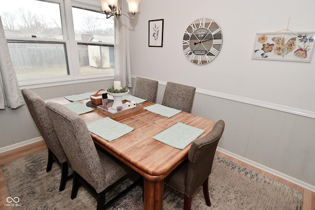 dining space with a wainscoted wall, a notable chandelier, and wood finished floors