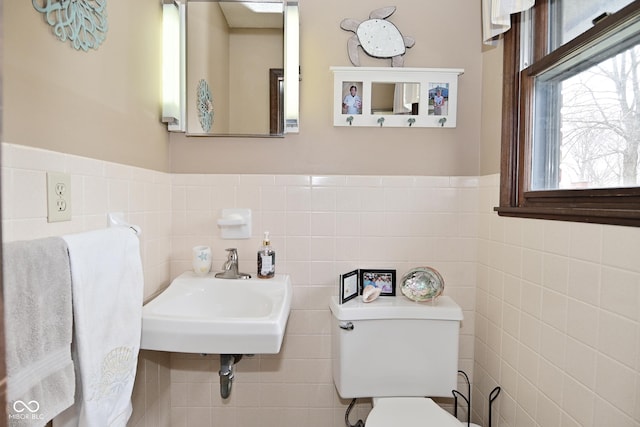 bathroom featuring wainscoting, a sink, toilet, and tile walls